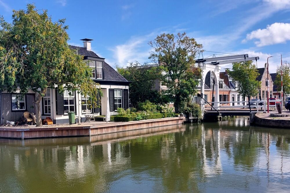 Witte ophaalbrug over het water in Makkum met een wit huis met zwarte luiken aan de kade