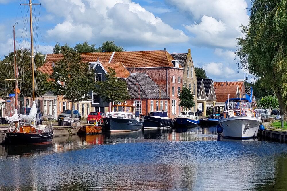 Boten afgemeerd in de vaart Grutte Sylroede in Makkum, met oude pakhuizen en woonhuizen langs de kade