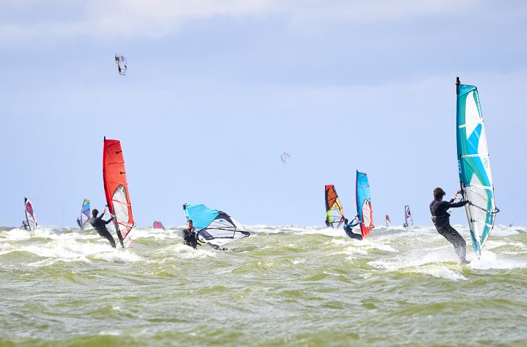 Windsurfers met gekleurde zeilen op het Strand de Holle Poarte in Makkum, met het ruime IJsselmeer op de achtergrond.